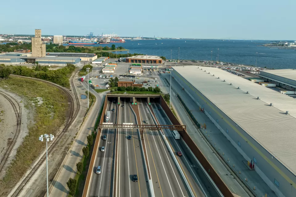 Aerial view of an eight-lane highway tunnel with the harbor in the background.